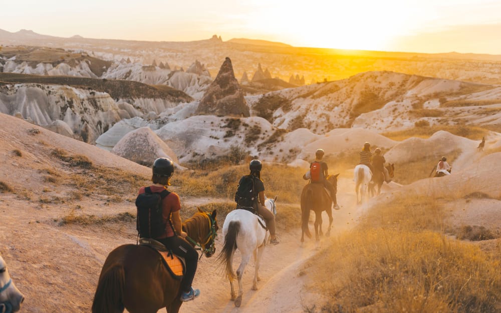 Horse riders following a valley trail in warm evening light