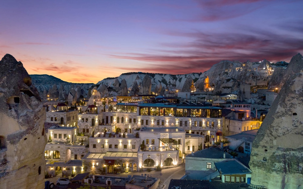 Carus Cappadocia and Göreme’s hillside buildings at dusk
